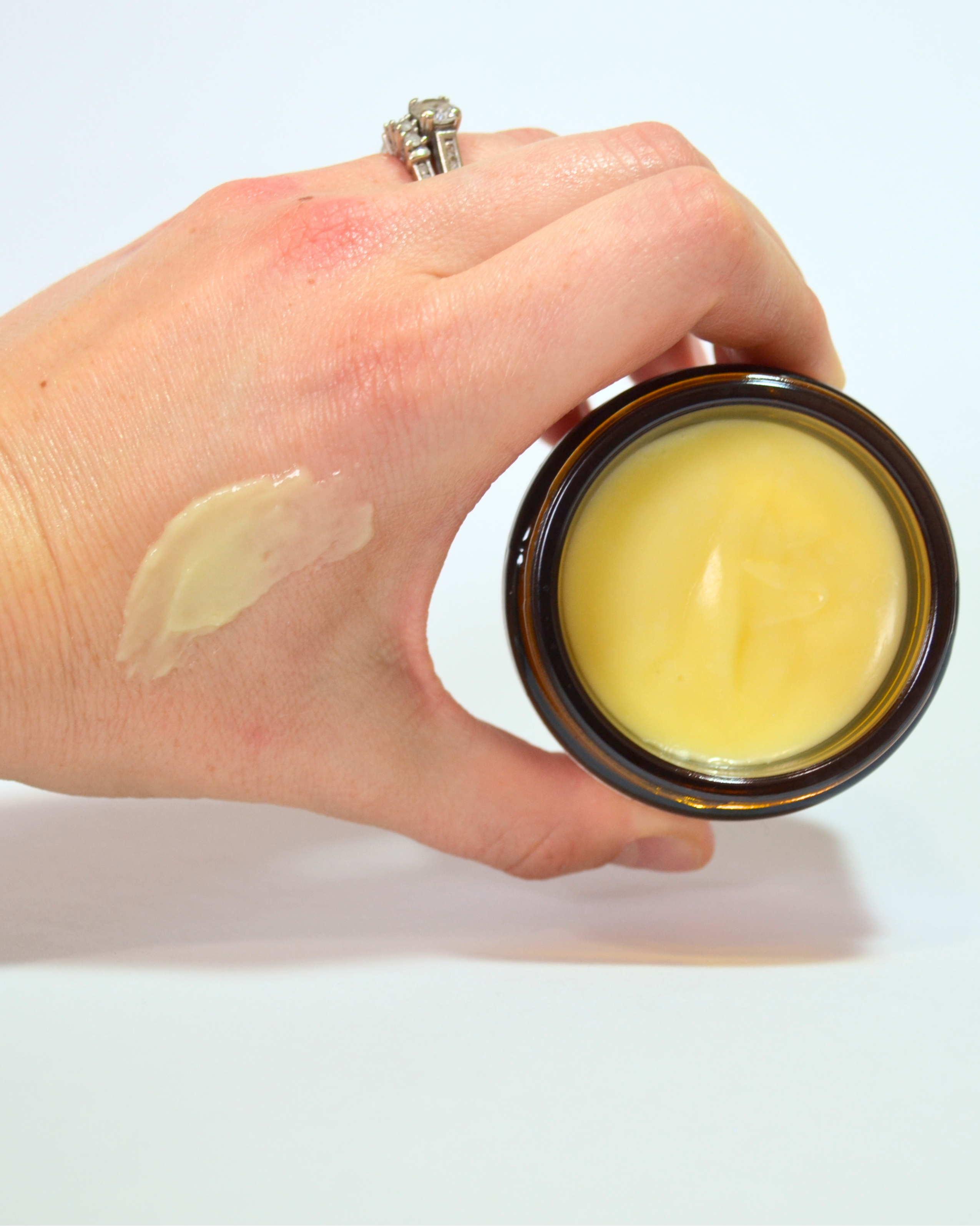 Hand holding a jar of yellow cream with a visible swatch on the skin.